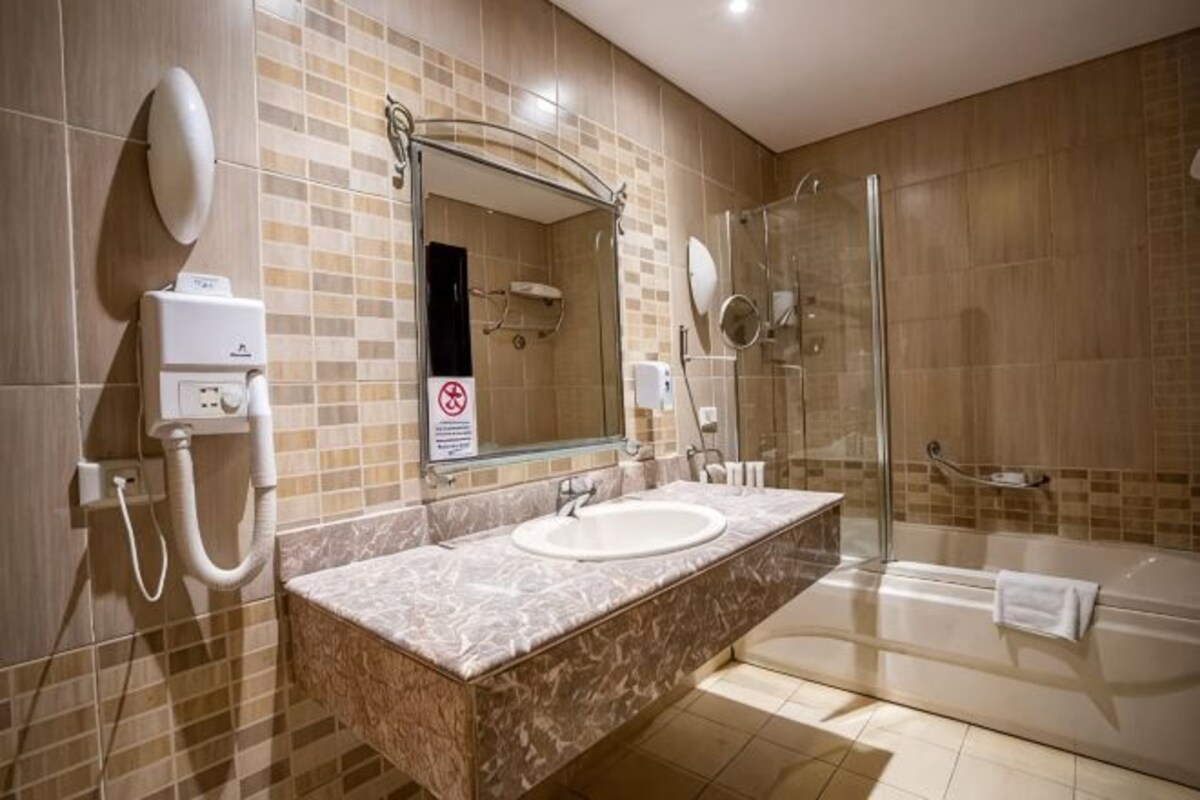 A bathroom with a marble sink, a mirror, a glass shower enclosure, and a towel rack.