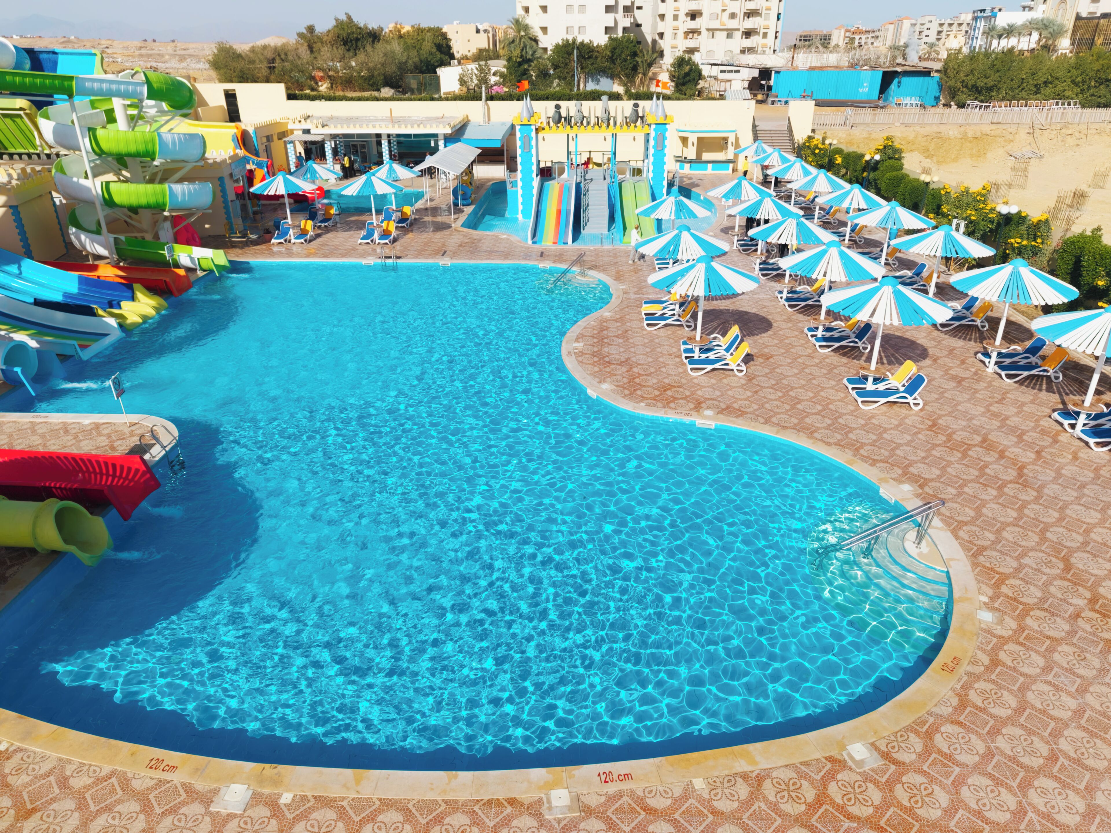 A swimming pool with a water slide, lounge chairs, and umbrellas.