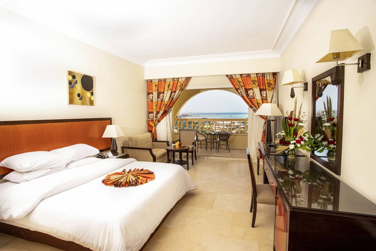 Quarto de hotel com cama, escrivaninha, cadeira, televisão e vista para o mar.