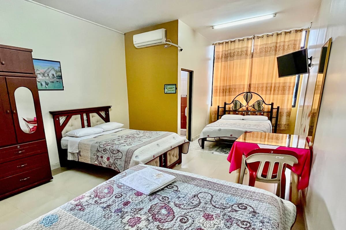 Un dormitorio con dos camas individuales, un armario de madera, un escritorio con silla, un televisor de pantalla plana y un aire acondicionado.