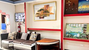 A hotel lobby with a sofa, a small table, a television, framed artwork, and a map on the wall. - Hotel Coca Imperial (Coca)