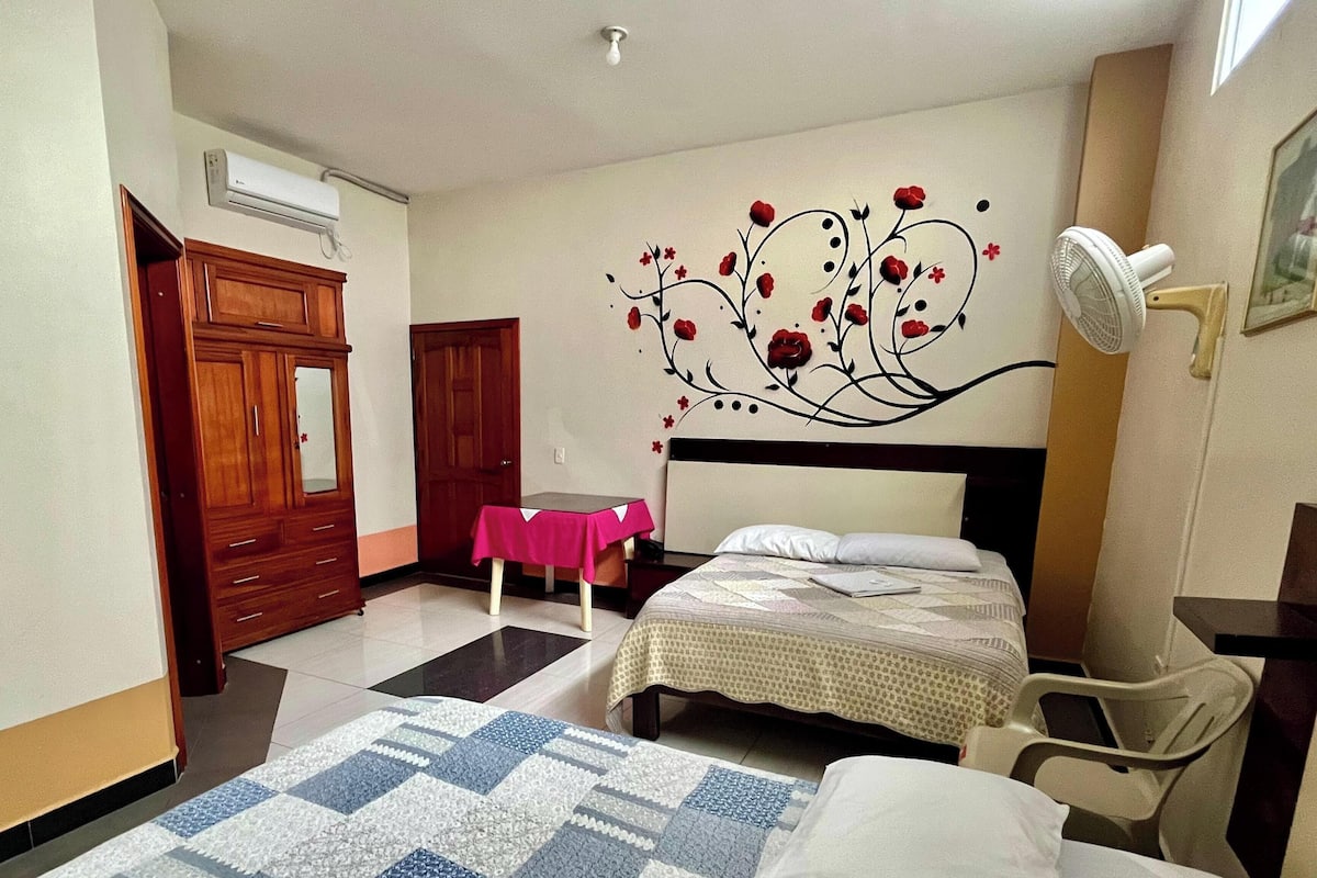 Un dormitorio con dos camas, un armario de madera, una mesa con mantel rosa y una decoración en la pared.