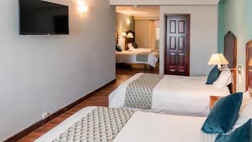 Habitación de hotel con dos camas, un televisor fijado a la pared, una puerta y una lámpara.