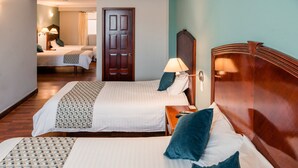 A hotel room with two beds, a wooden headboard, a bedside table with a lamp, and a door. - Hotel Libertador (Loja)