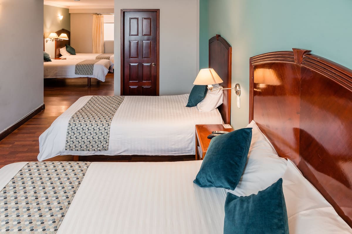 A hotel room with two beds, a wooden headboard, a bedside table with a lamp, and a door.