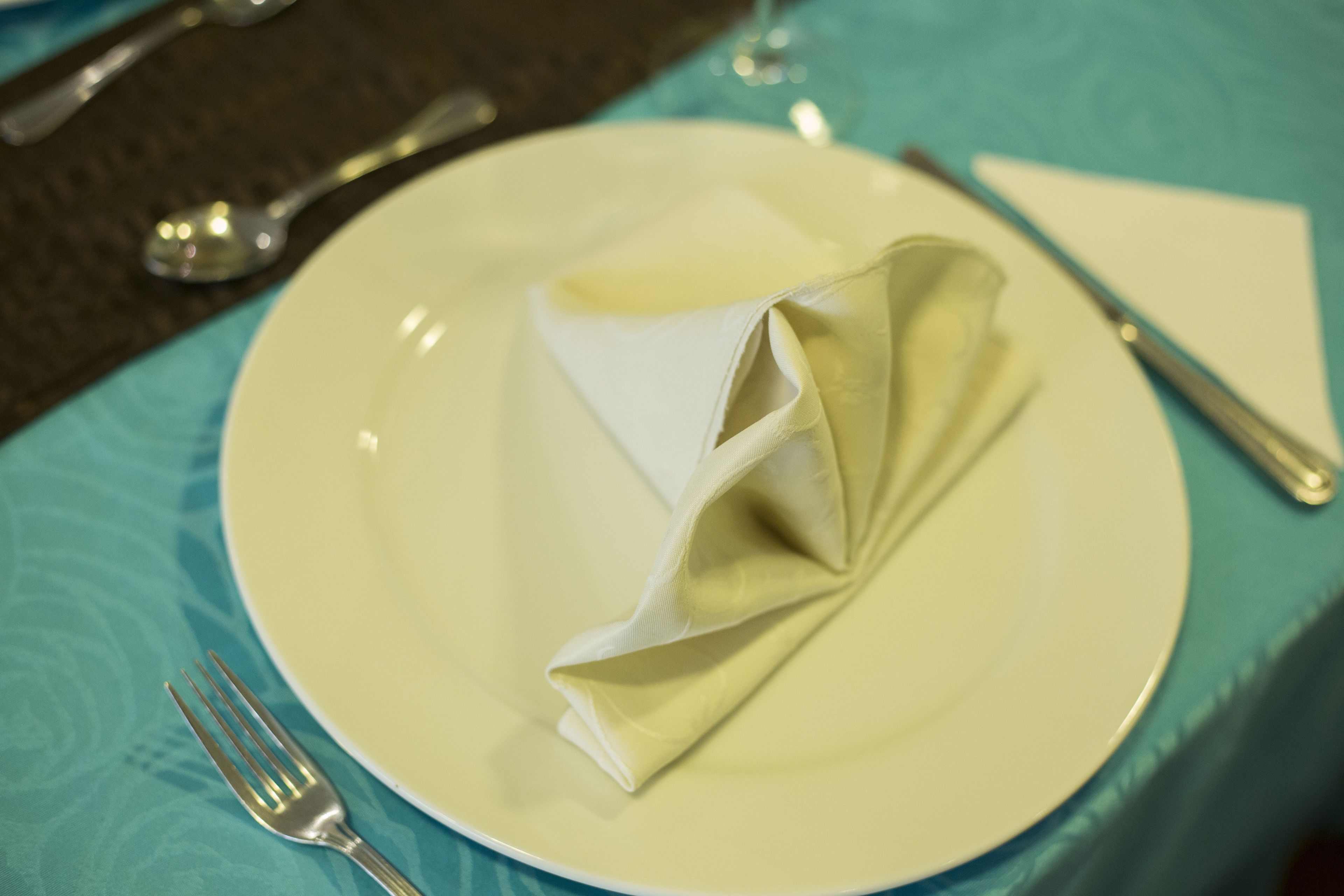 A plate with a folded napkin on a table with a fork beside it.