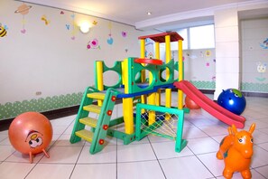 Zona infantil con una estructura de juegos colorida, que incluye un tobogán y escaleras de acceso.
