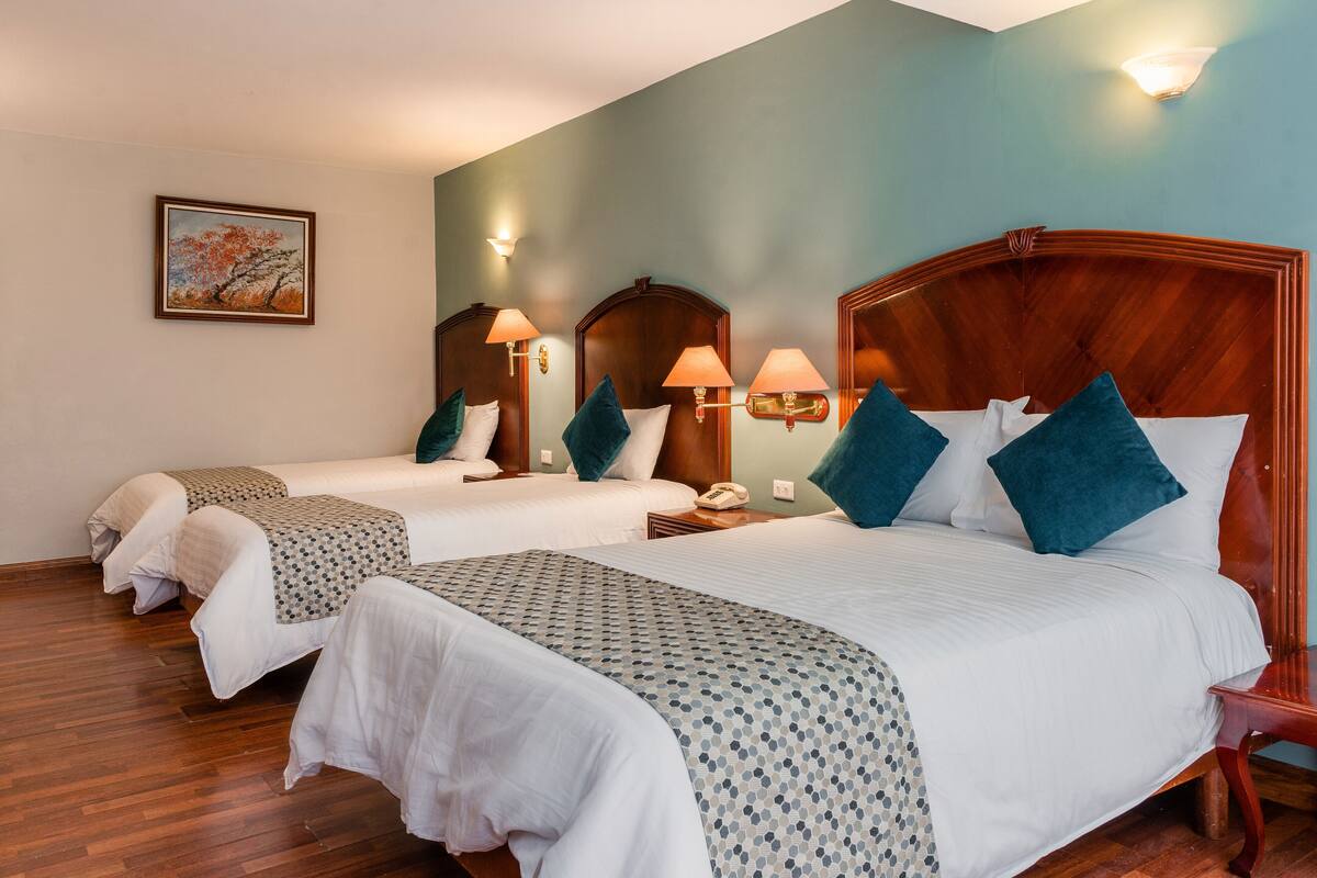 A hotel room with two single beds, a large bed, wooden headboards, and a painting on the wall.