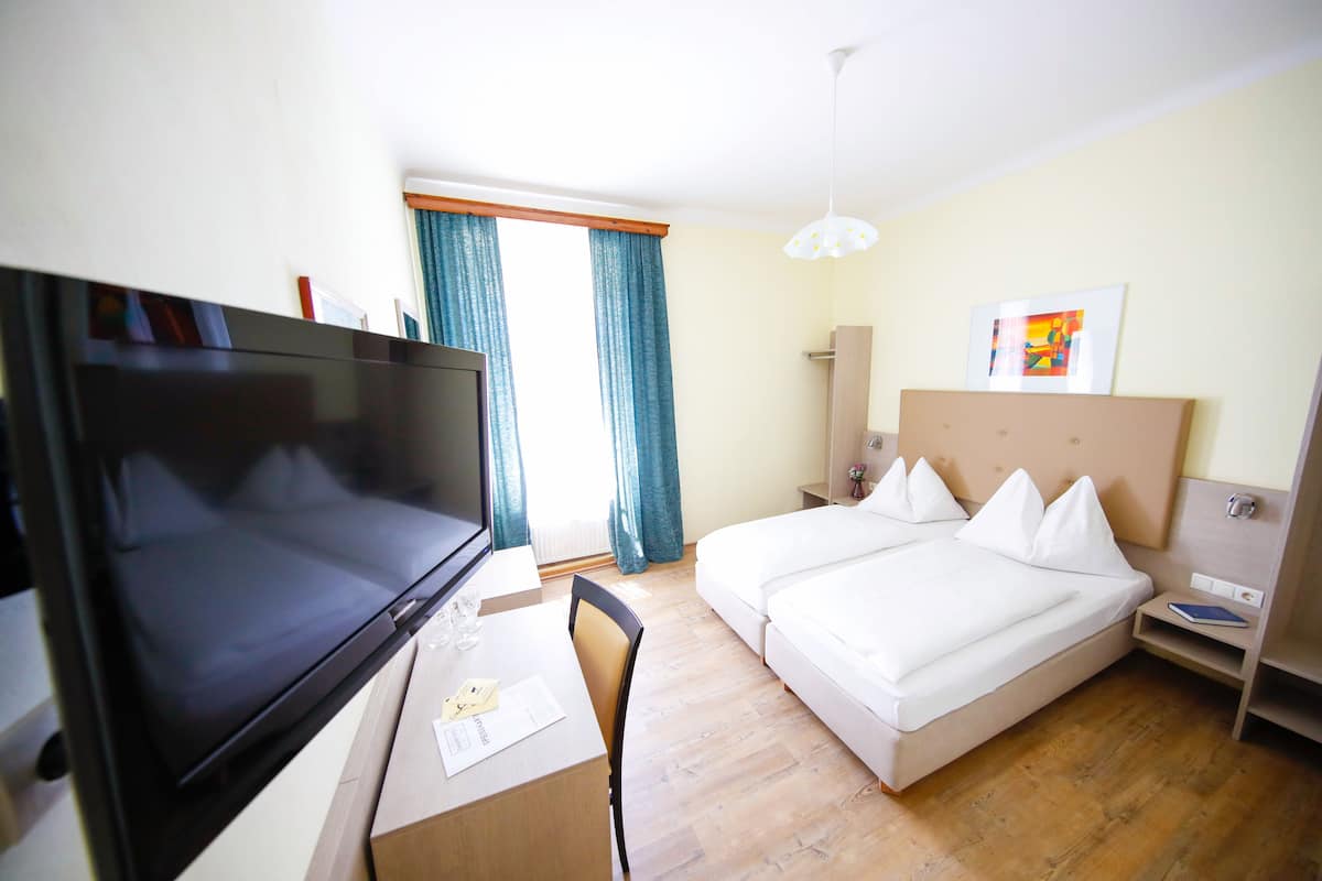 A hotel room with a bed, a desk with a TV, and a window with curtains.