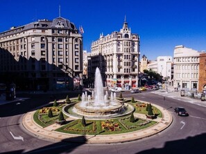 Una glorieta con una fuente en el centro, rodeada de jardines cuidados y diversos edificios, entre ellos un edificio blanco destacado con una cúpula.