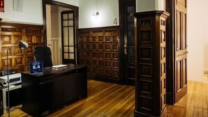 A hotel room with a wooden desk, a chair, a lamp, and a sign indicating the room rate. - Zentric Hostel (León)