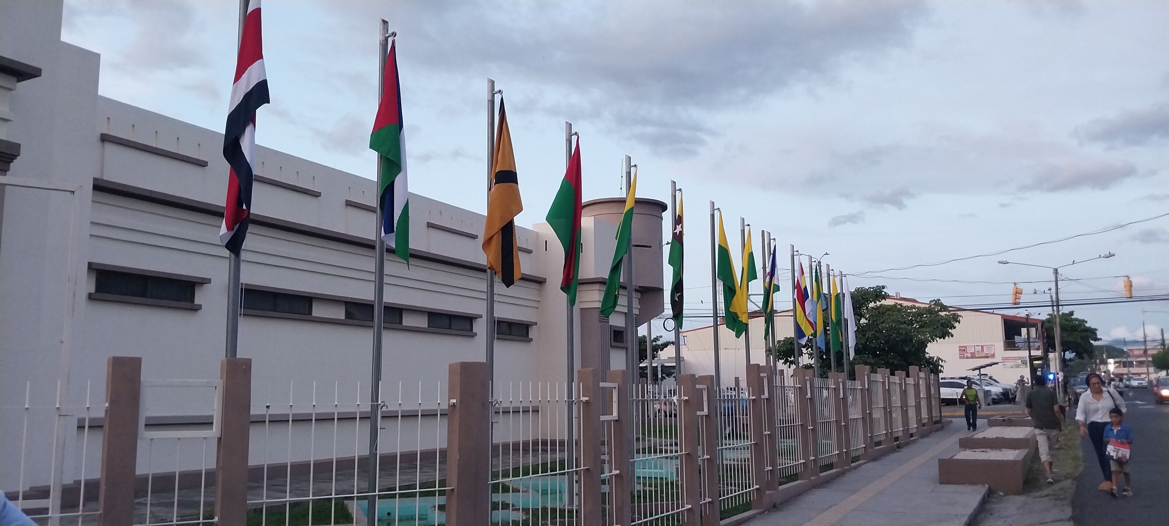 A row of flags on flagpoles in front of a building.