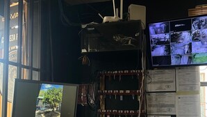 A home office setup with a desktop computer, two monitors, a telephone, and a shelf with multiple electronic devices and papers. - Hotel Guanacaste (Liberia)