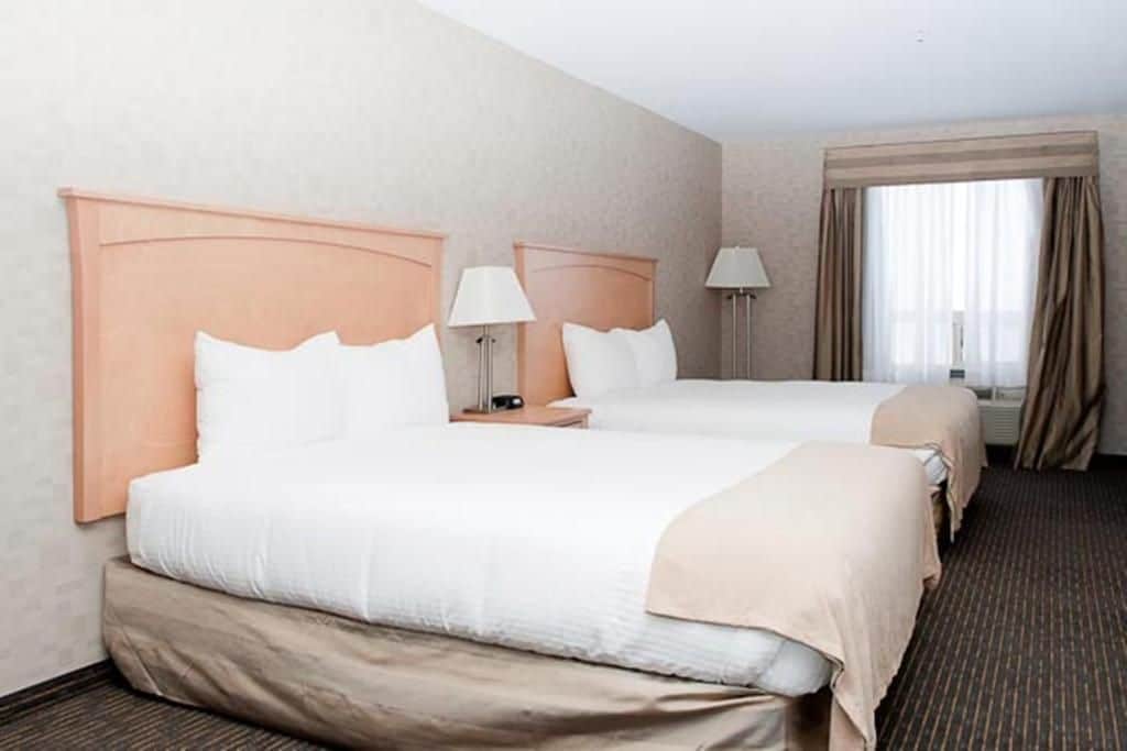 Una habitación de hotel con dos camas, una ventana con cortinas y una lámpara en cada mesita de noche.