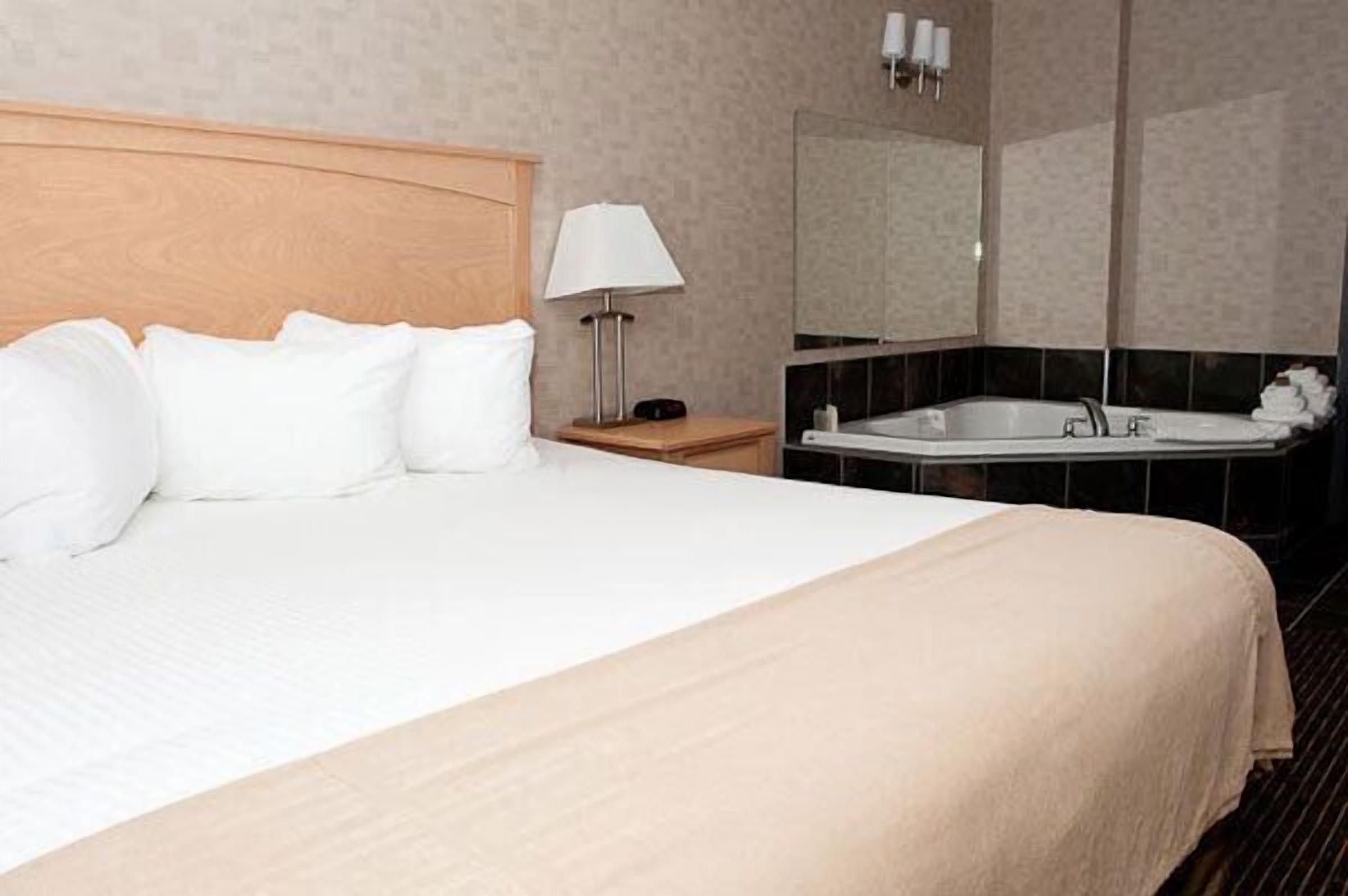 A hotel room with a large bed, a bedside lamp, a bathroom with a bathtub, and a mirror.