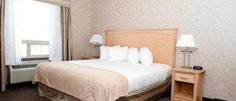 Habitación de hotel con una cama grande, dos lámparas de noche, una mesita de noche y un ventanal con cortinas.