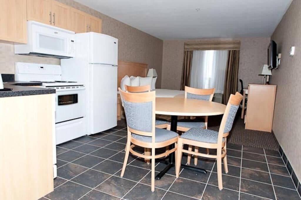 A compact kitchen with a stove, microwave, and refrigerator, a dining table with four chairs, and a small cabinet.