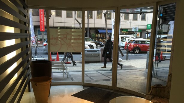 A hotel entrance with a glass door, a bench, and a table inside. - Senba Hostel (Osaka)