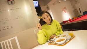 A person sitting at a table with a whiteboard, a glass of orange juice, and a tray with food. - Senba Hostel (Osaka)
