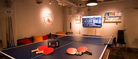 A ping pong table with paddles and balls, a TV mounted on the wall, and a chair.