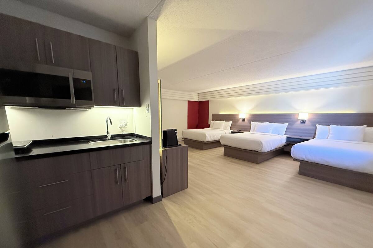 Een hotelkamer met een kitchenette, twee bedden en een rode accentmuur.