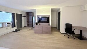 Ett modernt hotellrum med trägolv, ett skrivbord med en stol, en TV, en minibar och en garderob.