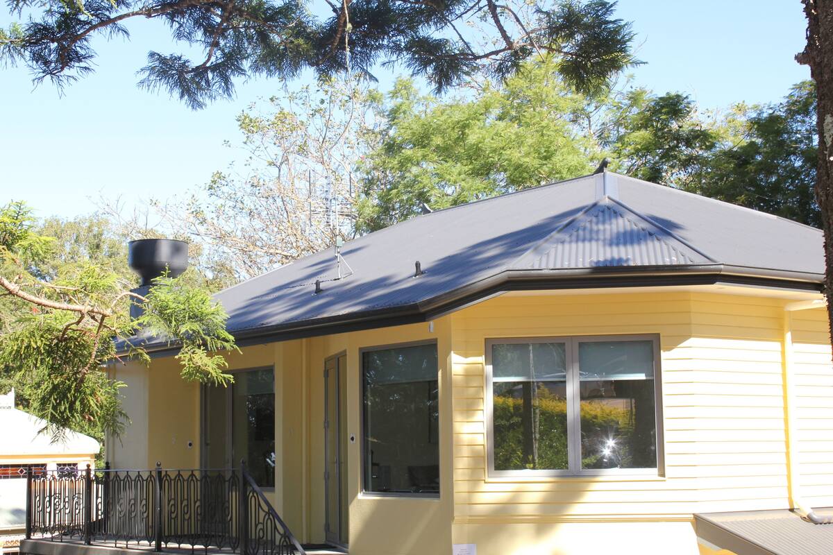 A yellow house with a dark roof, a black railing, and a window.