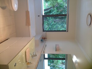 A modern bathroom with a large window, a bathtub, a sink, and a mirror.