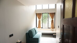 A room with a teal sofa, a bench, a window with curtains, and a wooden door. - De Halimun Guest House (Bandung)