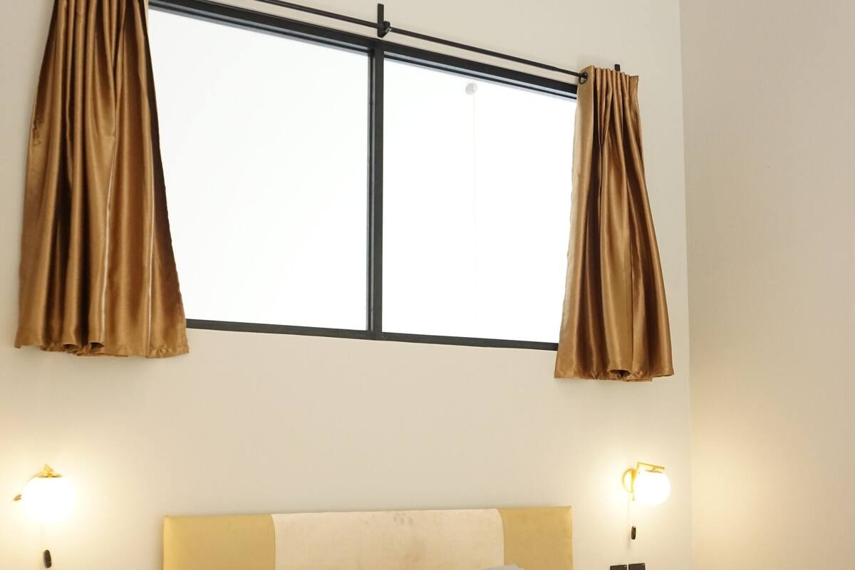 Een slaapkamer met een bed, gordijnen, wandlampen en een raam.