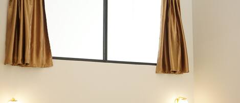 A bedroom with a bed, curtains, wall-mounted lights, and a window.