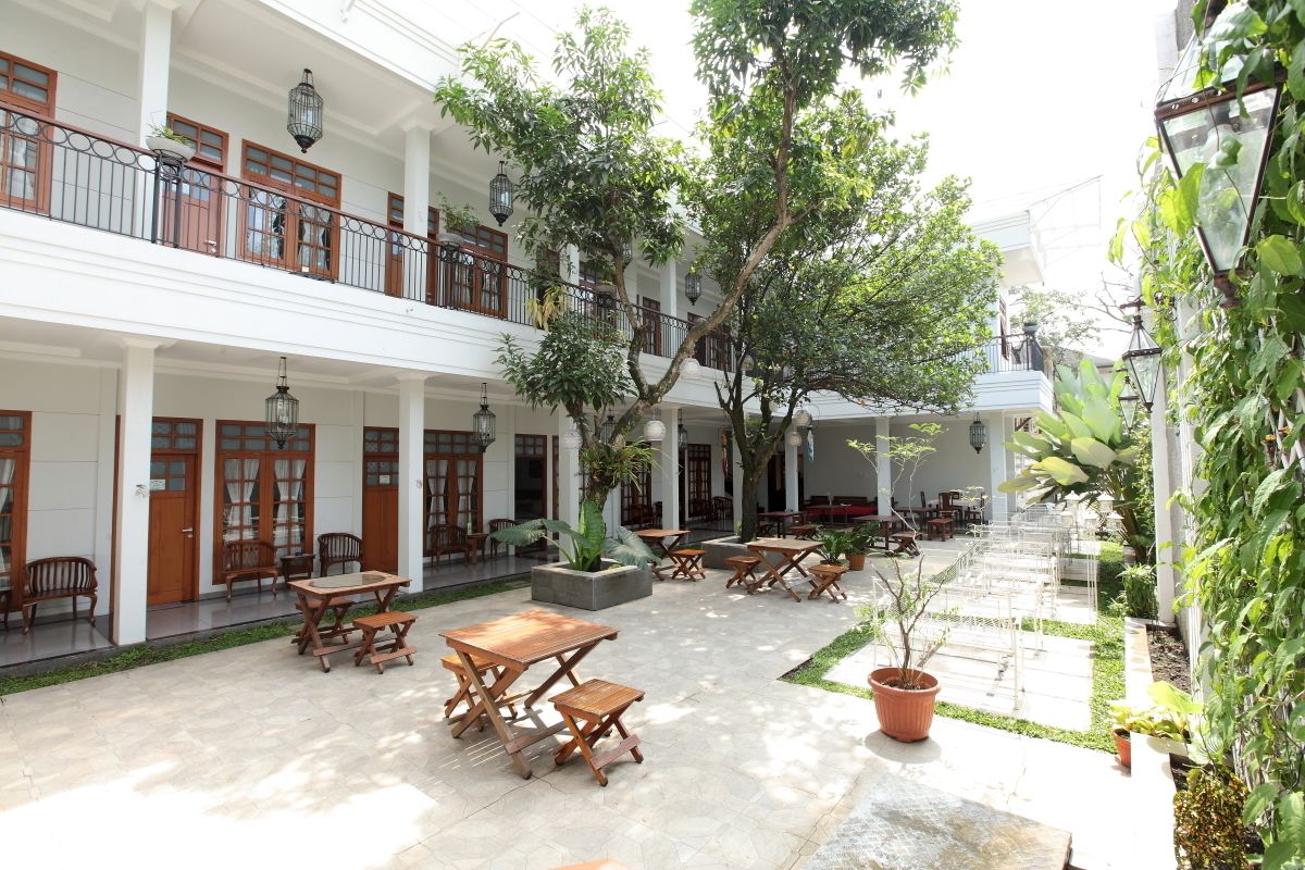 A courtyard with wooden tables and chairs, potted plants, and a large tree.