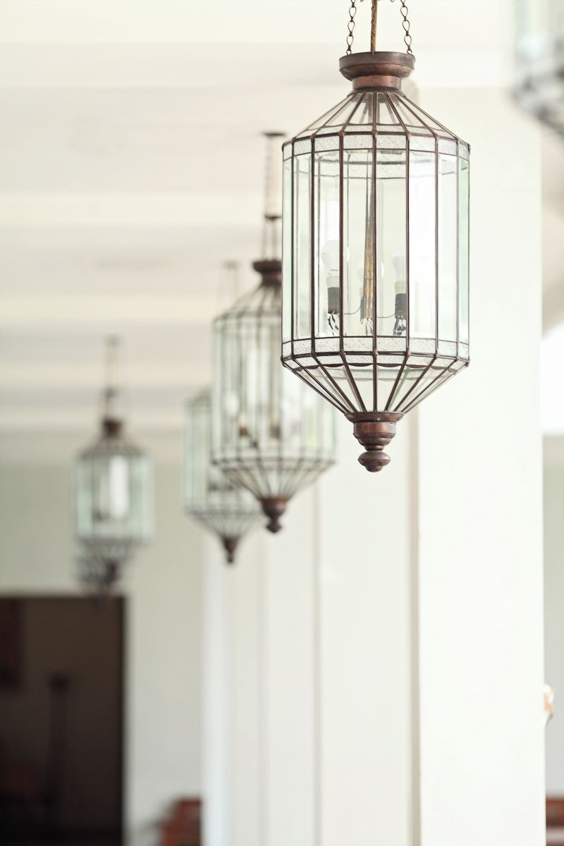 Une série de luminaires suspendus en métal, de style lanterne, avec une base en bois, fixés au plafond d’une pièce aux murs blancs.