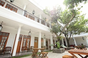 A multi-level courtyard with wooden furniture, a large tree, and hanging lanterns. - De Halimun Guest House (Bandung)