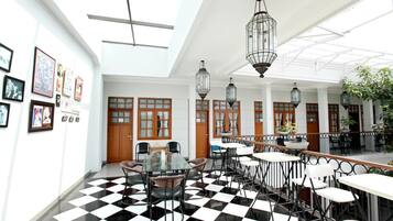 A spacious indoor area with a checkered floor, multiple tables and chairs, hanging lanterns, and framed pictures on the walls.