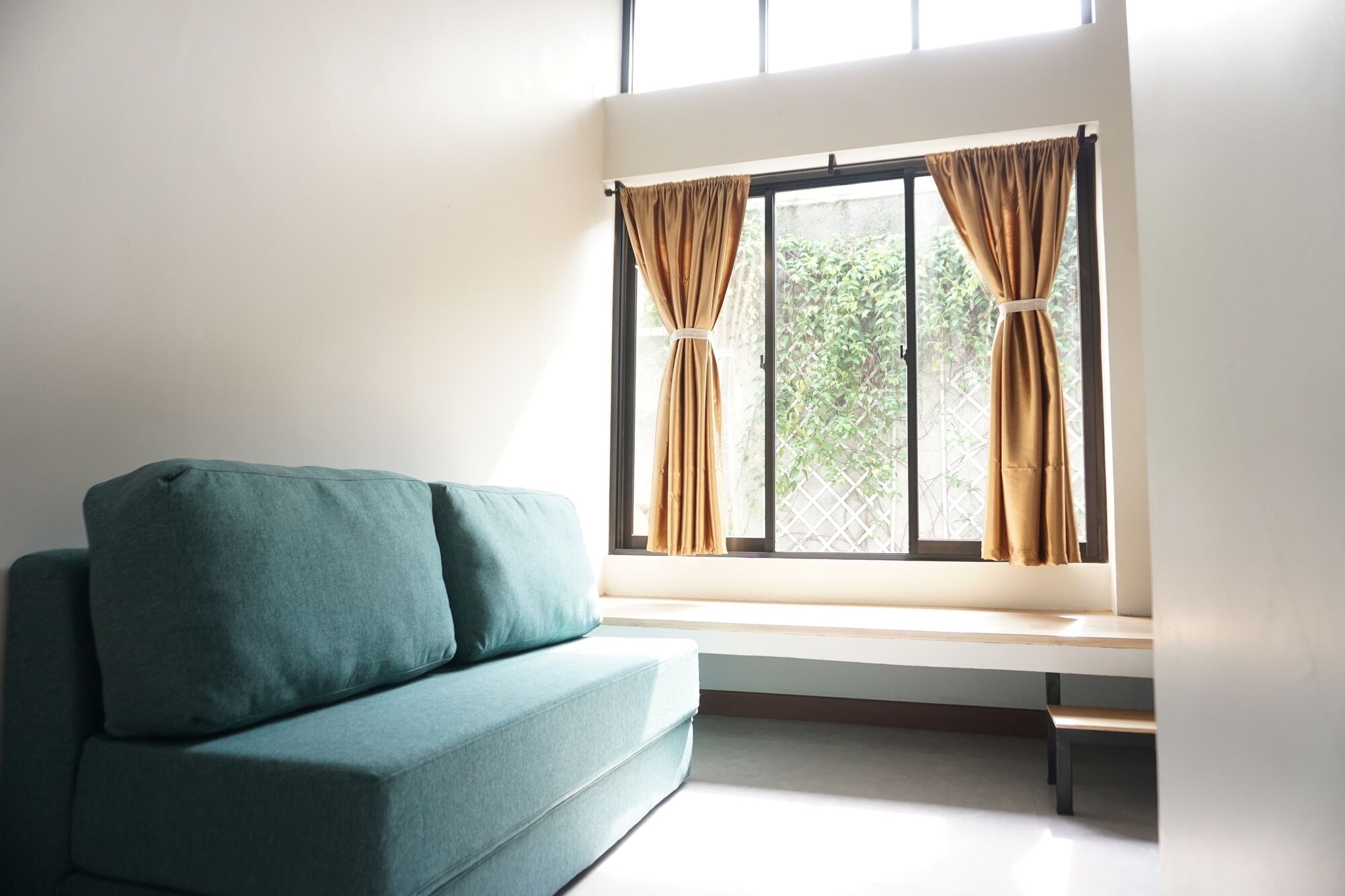 Una habitación con un sofá color turquesa, un banco y una ventana con cortinas.
