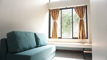 Um quarto com um sofá azul-esverdeado, um banquinho e uma janela com cortinas.