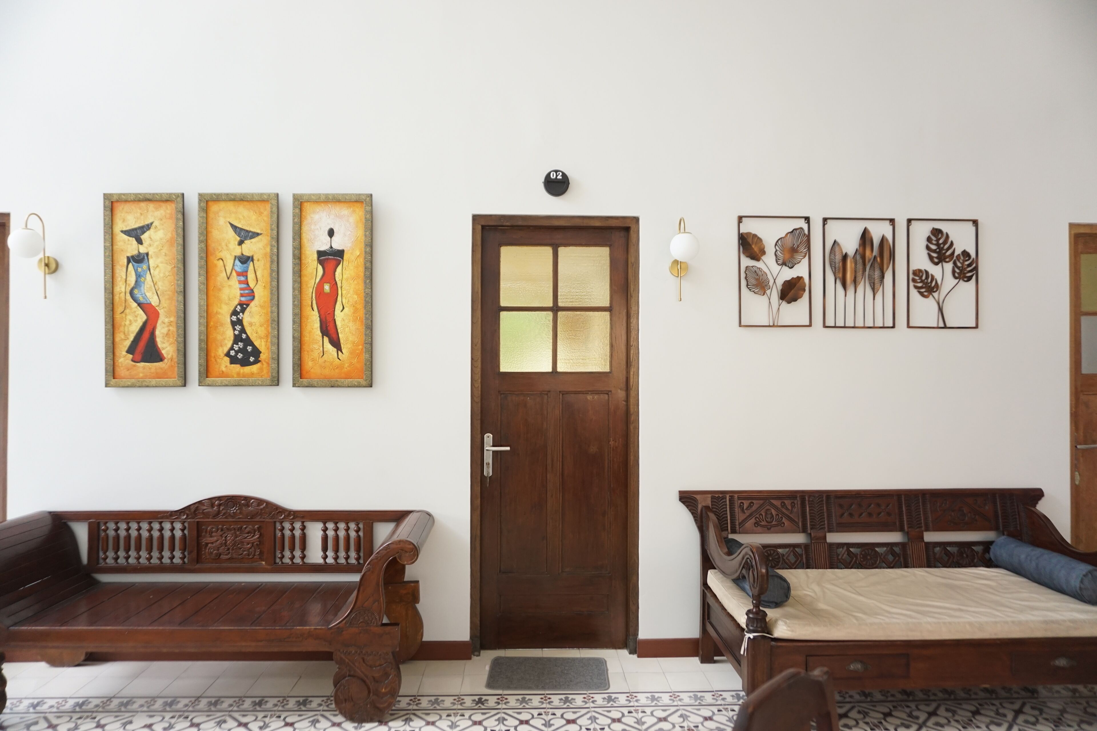 A room with a wooden door, a bench, a bed, and wall art.