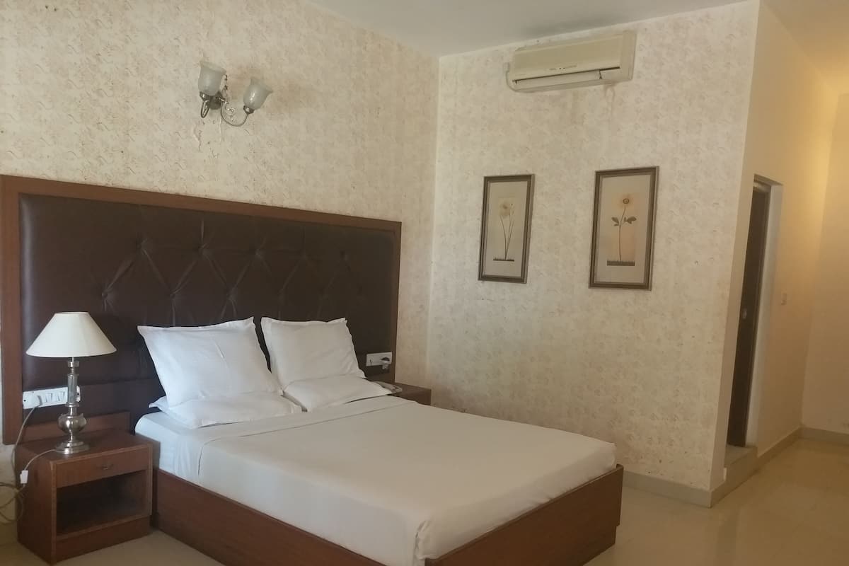 A neatly made bed with white linens, a wooden headboard, a bedside lamp, and two framed pictures on the wall.