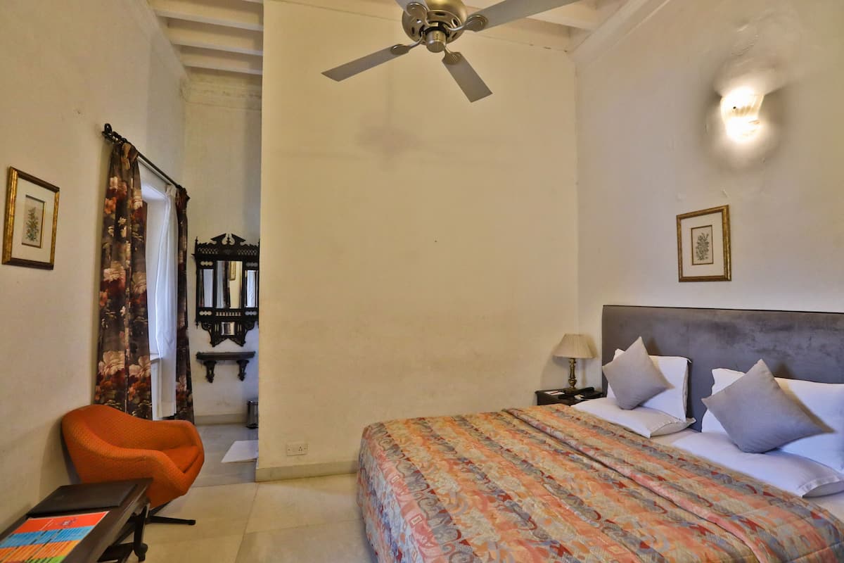 A hotel room with a bed, a chair, a ceiling fan, and a nightstand with a lamp.