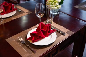 Una mesa de comedor con un mantelito rojo doblado, un plato blanco, un tenedor, un cuchillo y un vaso de agua.