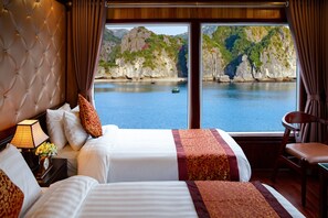 Habitación de hotel con un ventanal grande que ofrece vistas a la costa, con acantilados y un barco en el agua.