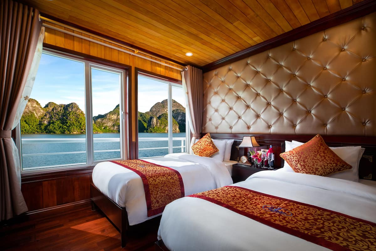 Habitación de hotel con dos camas, un ventanal con vistas a montañas y al agua, y techo de madera.