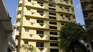 A multi-story yellow building with balconies, a paved ground floor, and a tree in the foreground. - Mookai Hotel (Male)