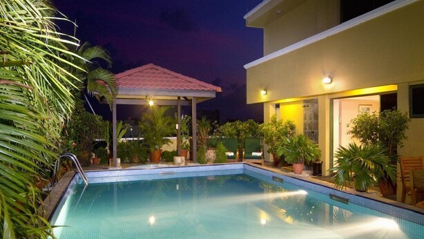 A swimming pool with a tiled deck, surrounded by potted plants and a covered area. - Mookai Hotel (Male)