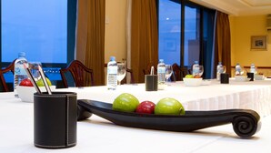 A conference table with water bottles, a bowl of fruit, and a black tray with apples. - Mookai Hotel (Male)