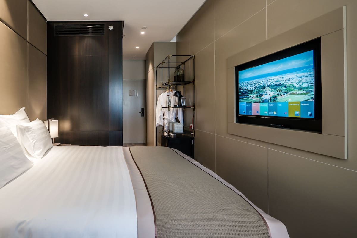 Una habitación de hotel moderna con una cama grande, un televisor montado en la pared y un estante pequeño con artículos de aseo.