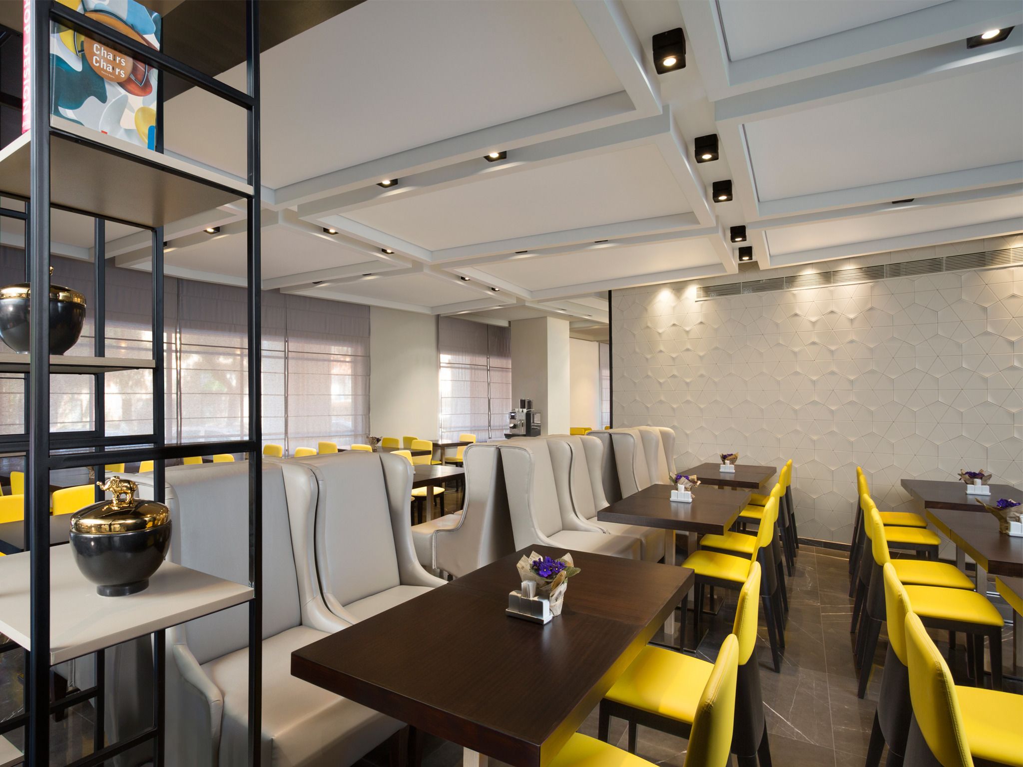 Un restaurante moderno con mesas altas y sillas amarillas, una zona de bar y una pared decorativa.