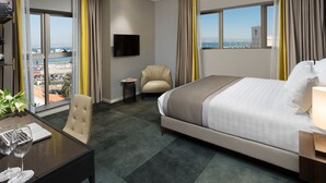 Ein Hotelzimmer mit einem Bett, einem Schreibtisch mit Laptop und Brille, einem Stuhl, einem kleinen Tisch und einem Fernseher an der Wand.