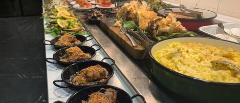 Un bufé con diversos platos, incluyendo pollo frito, ensaladas y una gran fuente de puré de papas.